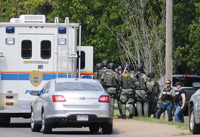 Members of a SWAT Team assemble before entering a house in Fayetteville on Sunday where they believed a suspect in the shooting might be. A woman was found in the front yard with a gunshot wound to the head.