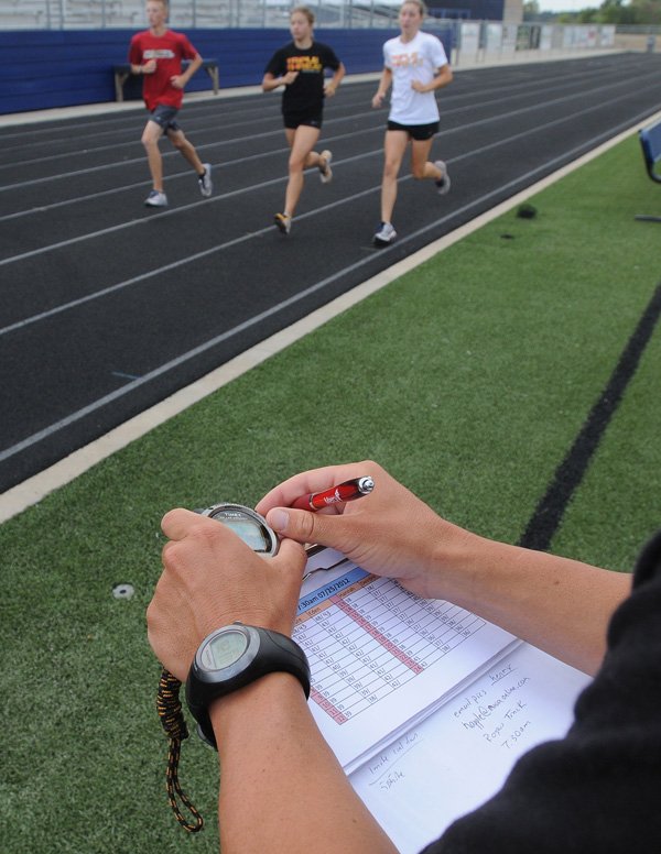 Shawn Wierick, head coach for Triple Threat Running, bottom, keeps track of times Thursday as Treyton Murphy, 14, from left, Eden Randolph, 15, and Deirdre Sheets, 16, run 200-meter sprints at Mountie Stadium in Rogers. Randolph and Sheets are two of five teammates competing at the junior elite level and are currently training for a national triathlon competition in West Chester, Ohio. The triathlon consists of a 750-meter swim, 20-kilometer bike ride, and finishes with a 5-kilometer run. 