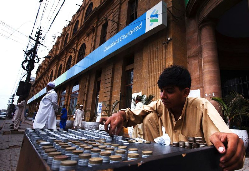 A money changer arranges coins outside a Standard Chartered Bank branch in Karachi, Pakistan, on July 30. New York’s state financial services superintendent on Monday requested that the bank answer questions as part of an investigation into financial transactions between the bank and Iran. 