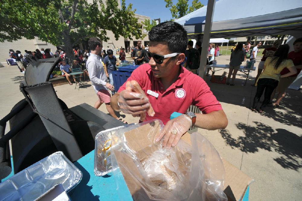 STAFF PHOTO MICHAEL WOODS --08/20/2012-- Rudy Trejo, advisor to the University of Arkansas Student Government, throws another box of hot dogs on the grill Monday afternoon as he helps grill up lunch for students as they return to the University for the first day of classes for the Fall of 2012.