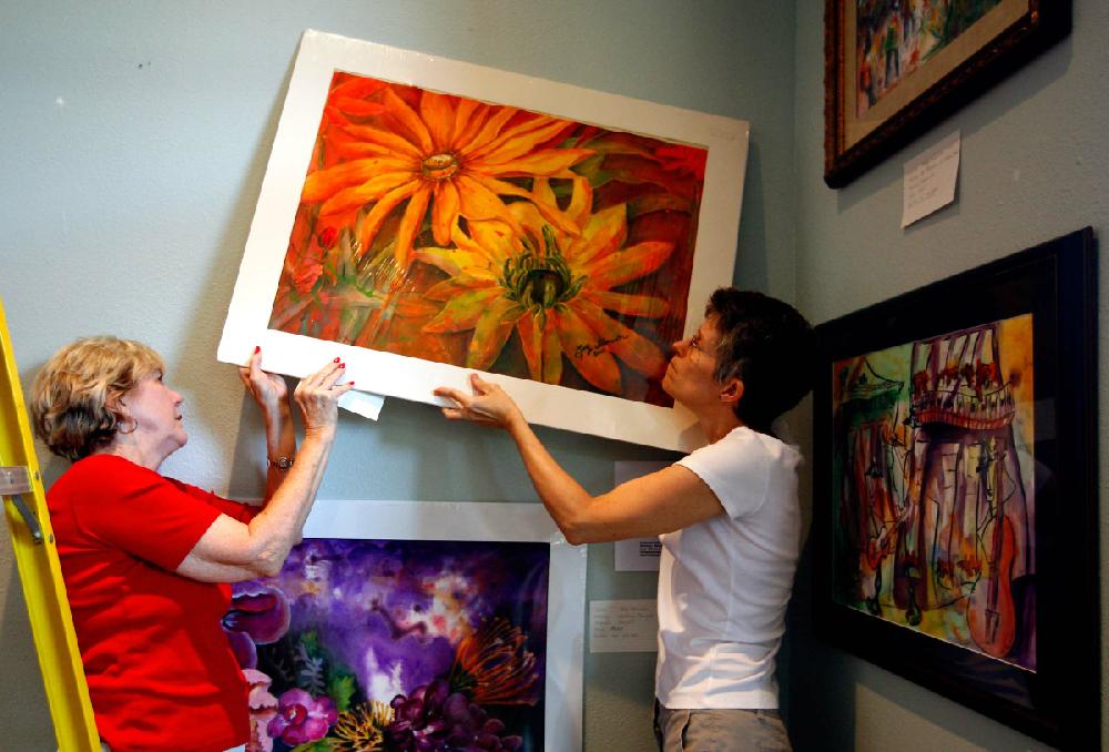 STAFF PHOTO JASON IVESTER
Betty Shewmaker (left) of Rogers and Beth Myers of Rogers work to hang one of Shewmaker's art pieces inside a temporary gallery on Monday, Aug. 20, 2012, at the Village on the Creeks in Rogers. Over 50 artists are displaying their works for the Art on the Creeks art walk on Thursday. The event is free to the public and will also feature music from the Symphony of Northwest Arkansas.