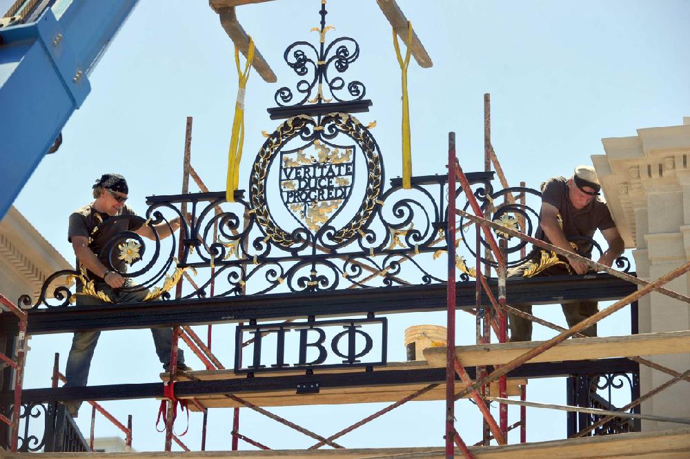 STAFF PHOTO MICHAEL WOODS --08/20/2012-- Othmar Briggl (left) and Dade Hauser both with Leonard Metal Art Works Inc. work on installing the top portion of the Pi Beta Phi Centennial Gate Monday afternoon at the University of Arkansas in Fayetteville. The gate is expected to be officially dedicated Sept. 21