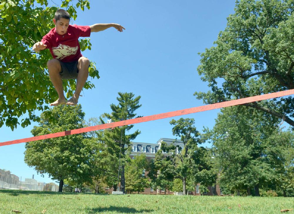 STAFF PHOTO MICHAEL WOODS --08/20/2012-- University of Arkansas sophomore Jimmy Barber catches some air as he works on his slack lining skills in front of Old Main on the University of Arkansas campus Monday afternoon. Monday was the first day for University of Arkansas students.