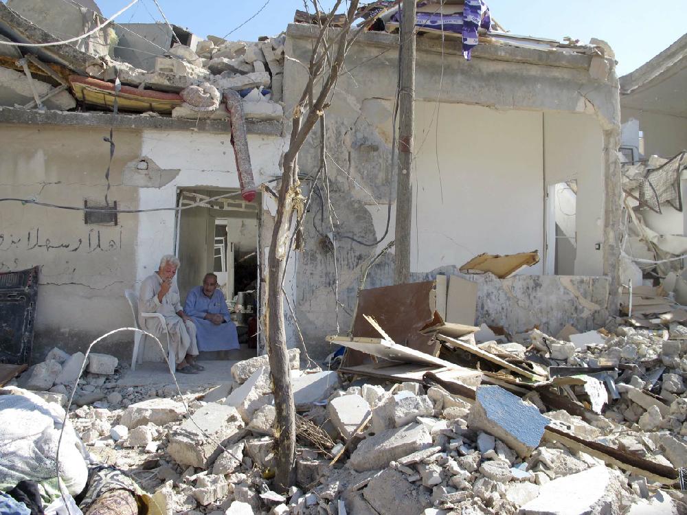 Syrians Bassem Kharfani, left, and Mahmoud Jikar sit at the door of Jikar's house, one of more than a dozen homes destroyed in a Syrian government bombing last week that killed more than 40 people, in Azaz, Syria, Monday, Aug. 20, 2012. (AP Photo/Ben Hubbard)