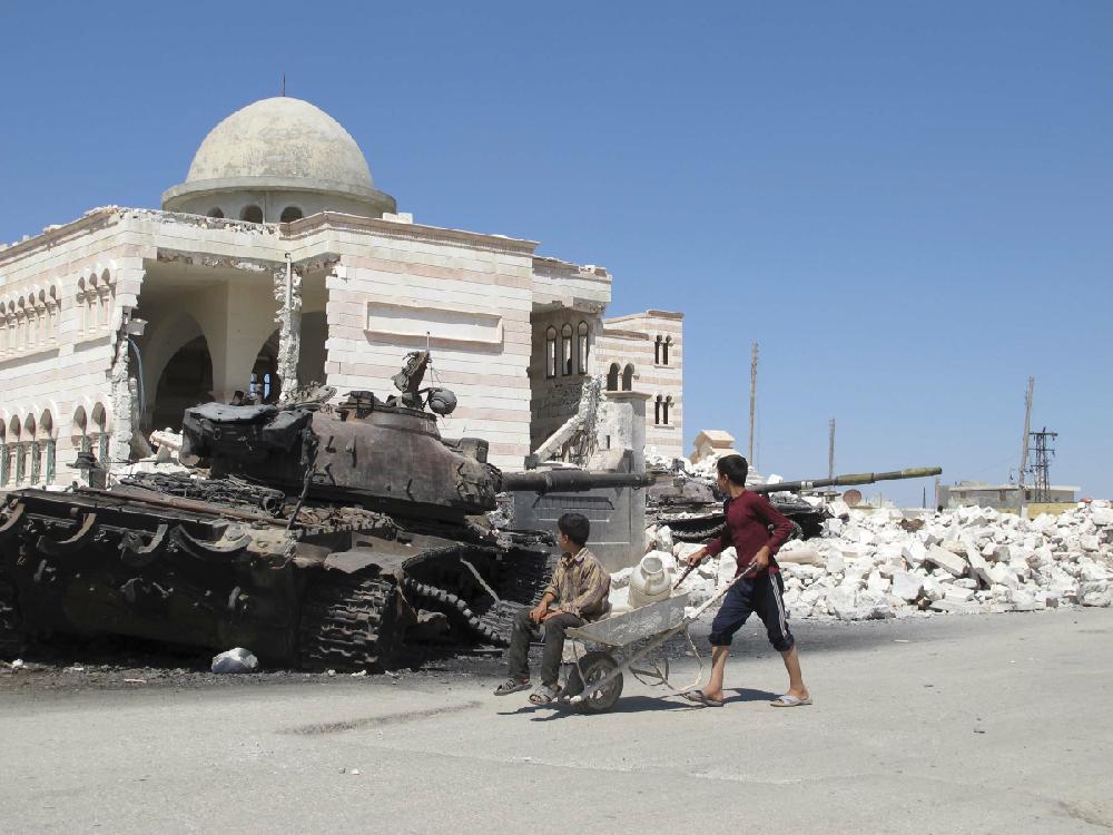 Syrian boys fetching water in a wheelbarrow look at a destroyed Syrian tank near a damaged mosque in the city of Azaz, Syria, on Monday, Aug. 20, 2012. (AP Photo/Ben Hubbard)