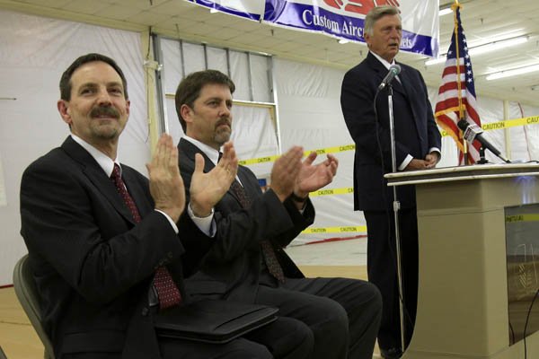 Custom Aircraft Cabinets Inc. owners Mike Gueringer (left) and Paul Reesnes (center) applaud as Gov. Mike Beebe speaks Friday in Sherwood during a news conference to announce plans for 150 new jobs at the company.