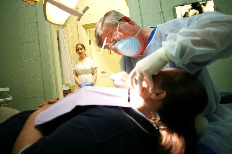 Arkansas Democrat-Gazette/RYAN MCGEENEY --07-11-2012-- Angela Heston of Cassville, Mo., 16, left, watches from the hallway as dentist Don Eckard, right, performs a tooth extraction Wednesday on patient Lisa Lynn of Fayetteville in one of the Samaritan Community Center's two cramped dental exam rooms. Heston, a volunteer, has been receiving on-the-job training as a dental assistant through the center. Eckard, who began practicing dentistry in 1972 and is now in self-described "semi-retirement," is one of about a dozen dentists and oral surgeons who volunteer their services for low-income Arkansas residents through the Samaritan Community Center.