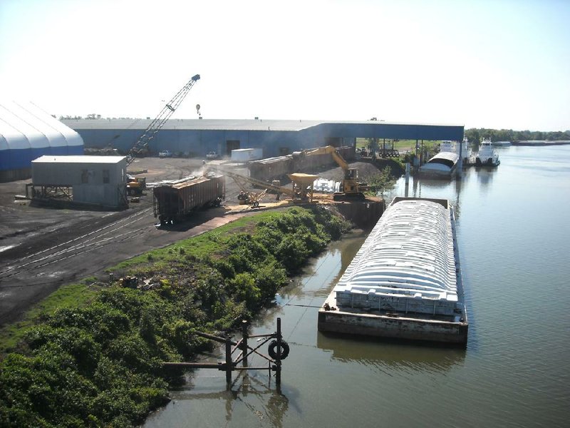 A yellow material handling excavator scoops corn out of a barge and dumps it into a cute that leads to a railroad car at the Five Rivers Distribution Intermodal Facility on Sept. 7 in Van Buren. The port on the Arkansas River has seen a slight slowdown in activity because barge traffic was halted briefly due to low levels on the Mississippi River near Greenville, Miss.          