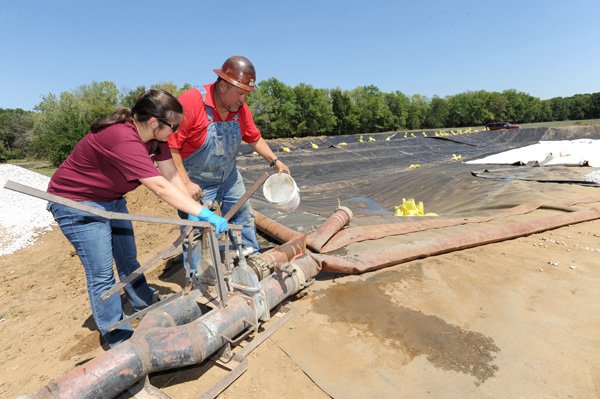 Nicole Wasko, left, of Ashland Chemical Co. in Dallas, and Tom Howard of Sludge Technology in Muskogee, Okla., look over a sample of sludge collected Wednesday on the eastern edge of Lake Sequoyah in Fayetteville as work continues to dredge the lake.