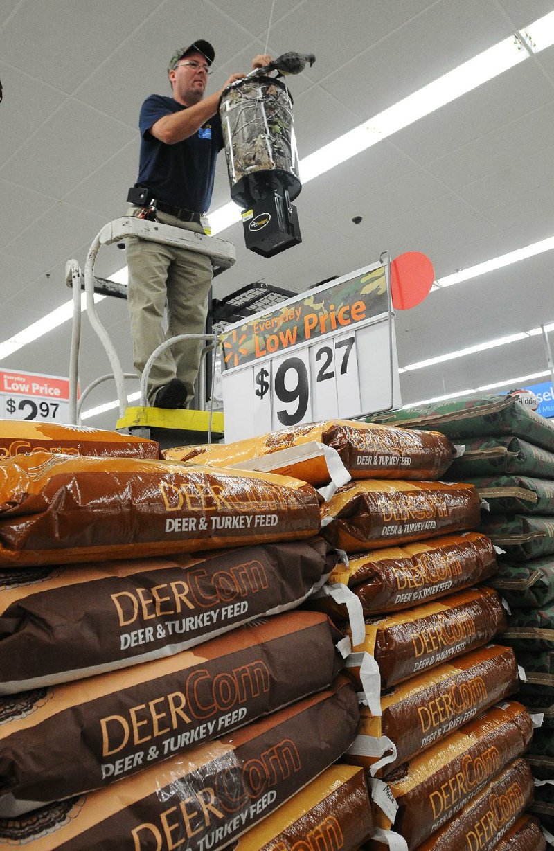 Employee Ron Rossicoe works on a display over sacks of deer corn Tuesday at the Wal-Mart on Walnut Street in Rogers. 