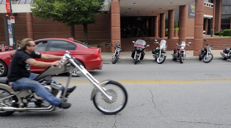 A motorcycle passes by a line of parked cruisers on Dickson Street on Sept. 13. Thousands of riders will invade Fayetteville during the Bikes, Blues & BBQ rally, which begins Wednesday. 