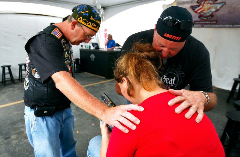 Jim May (from left) of Ardmore, Okla., Kristina Cole-Harris of Fayetteville and Richard Prather of Chickasha, Okla., pray together Wednesday inside the FAITH Riders tent on the Walton Arts Center parking lot in Fayetteville. The group is participating in the Bikes, Blues and BBQ motorcycle rally, which runs through Saturday in Fayetteville. 