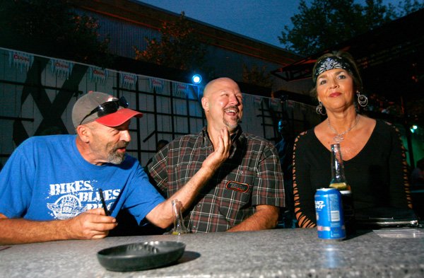 Roger Kelley, from left, of Springdale, Allan Reed of Fayetteville and Tonya Anderson of Fayetteville hang out Thursday and listen to live music by The Brothers Shreve at The Rogue on Dickson Street during Bikes, Blues & BBQ in Fayetteville. The bar hosted a private party for Harley Owners Group during the evening. 