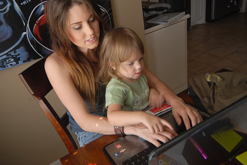 Nicole Almond sits at her laptop with her daughter, Aimslee. Almond works from her laptop on the kitchen table to be able to better watch her daughter.