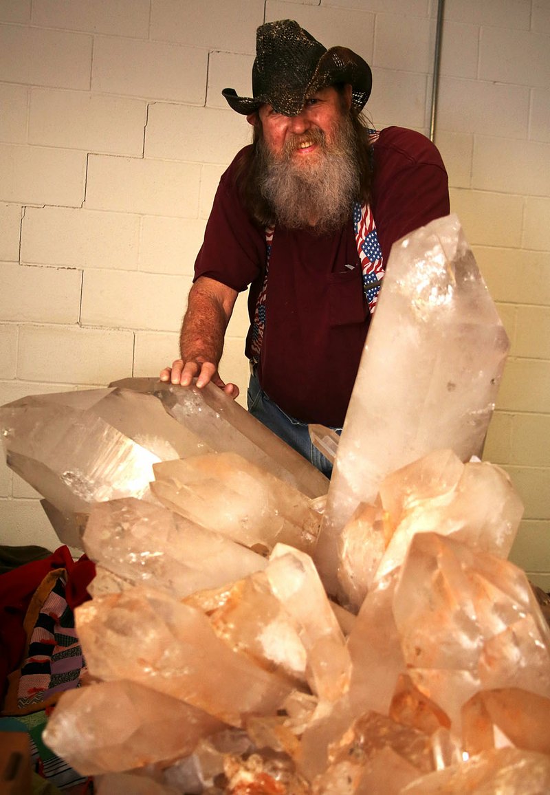Jim Coleman, owner of Jim Coleman Crystal Mines in Jessieville, stands behind a large quartz crystal cluster, only half of which is showing. Clusters of this size and quality have been known to sell for as much as $1 million or more. 