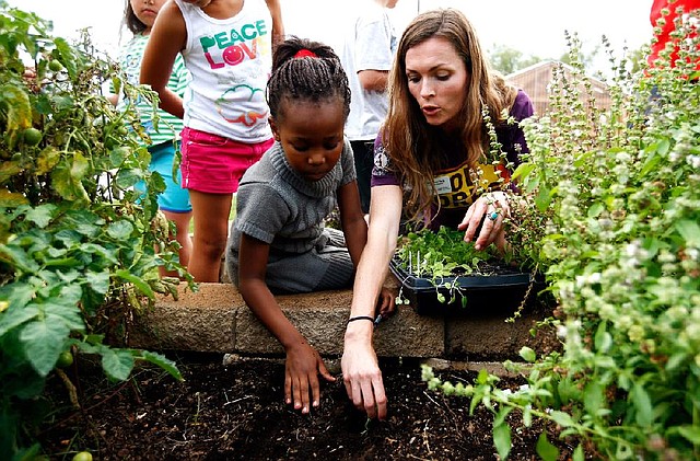 FoodCorps service member Allyson Mrachek helps Owl Creek School second-grader Rachel Sello, 7, plant vegetables in the school garden. Gardening programs are growing, giving students hands-on experiences that go beyond scratching in the dirt to science experiments and cooking classes. 