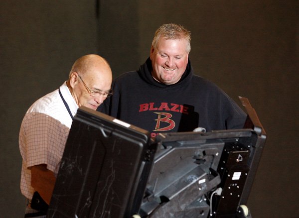 Jerr Feguson, left, voting machine operator, helps start the device for Mike Bray of Bentonville to cast his vote.