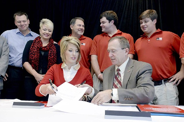 Meagan Uekman, sister of late Arkansas Razorbacks tight end Garrett Uekman, and University of Arkansas Athletic Director Jeff Long sign the official paperwork for the $100,000 scholarship in the memory of Uekman, who died in 2011 due to complications from cardiomyopathy. Also pictured are John Bennett, Uekman’s uncle; parents Michelle and Danny Uekman, and two of Garrett’s close friends, Chase Miller and Clark Morse. 