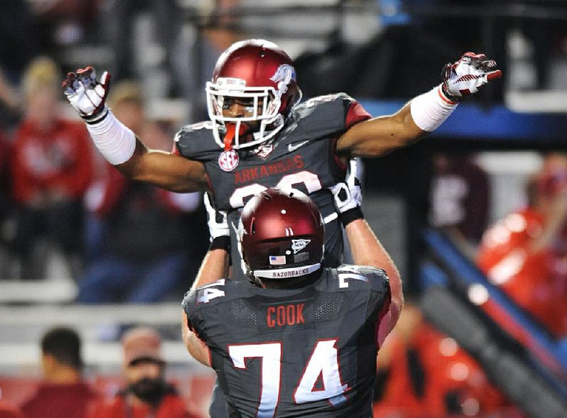 Arkansas offensive lineman Brey Cook (74) holds up running back Dennis Johnson after Johnson scored a second-quarter touchdown in Saturday’s game at Reynolds Razorback Stadium in Fayetteville. 