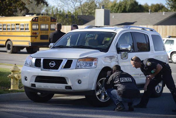 Glenn Bertand, left, police crime scene investigator, and Officer Andy Ball inspect damage to a vehicle Thursday that struck a Washington Junior High School seventh-grader on East Central Avenue and Jay Court in Bentonville. The condition of the boy hasn’t been released.