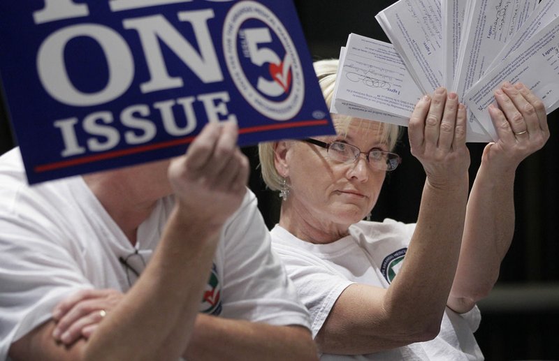 Melissa Fults, treasurer for Arkansans for Compassionate Care, holds up cards at the back of a room where a news conference is taking place at Baptist Health Medial Center in Little Rock, Ark., with the names of who she says are doctors who support a ballot issue that would legalize medical marijuana Wednesday, Oct. 24, 2012. The news conference was held by physicians who oppose the measure.