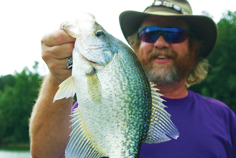 A hefty black crappie from Lake Greeson draws the attention of people looking at this photo. In the background is the person who caught it, writer Keith Sutton. While his nickname is “Catfish,” Sutton readily admits that a simple cane pole and crappie fishing can make him a very happy man.