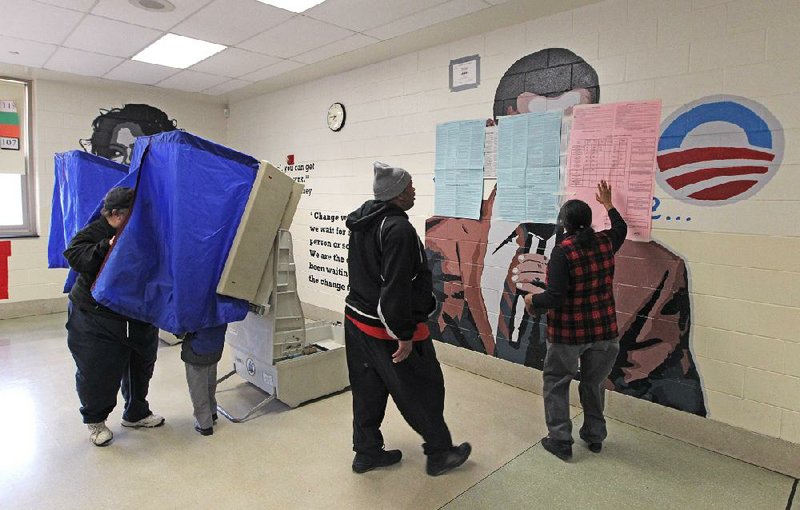 A poll worker (right), shows a voter a sample ballot that is covering a mural of President Barack Obama in the voting area of Benjamin Franklin Elementary School polling site Tuesday in Philadelphia. The mural was ordered to be covered after Republicans filed a complaint. 