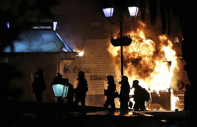 Greek riot police officers and members of the media stand next to a burning bus ticket kiosk near the parliament during clashes in Athens on Wednesday Nov. 7, 2012. Greece fragile coalition government faces its toughest test so far when lawmakers vote later Wednesday on new painful austerity measures demanded to keep the country afloat, on the second day of a nationwide general strike. The euro13.5 billion ($17.3 billion) package is expected to scrape through Parliament, following a hasty one-day debate. (AP Photo/Lefteris Pitarakis)