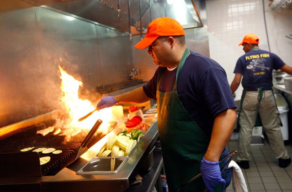 Oscar Garcia grills fish in the kitchen Friday during lunch at the Flying Fish restaurant in downtown Bentonville. 