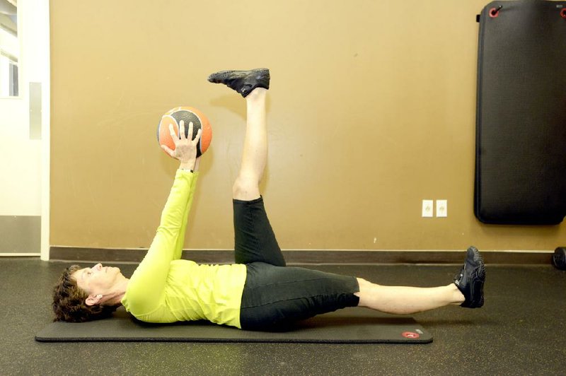 Nancy Jeffery contracts her abdominals to prevent her lower back from moving as her legs come up for the Straight Leg Scissors With Medicine Ball. 