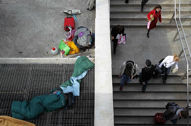 A homeless person sleeps on a subway ventilation grill Monday in Athens as commuters enter Syntagma station. Greece is waiting for the next $40 billion installment of its bailout loan before it faces a bond repayment due Friday. 