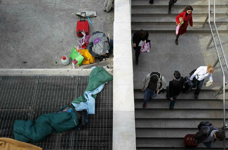 A homeless person sleeps on a subway ventilation grill Monday in Athens as commuters enter Syntagma station. Greece is waiting for the next $40 billion installment of its bailout loan before it faces a bond repayment due Friday. 