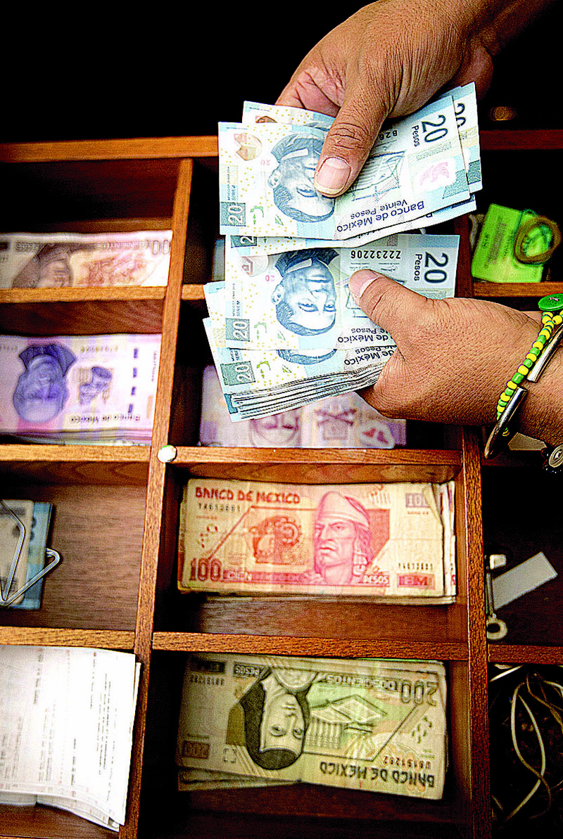 An employee at a currency exchange in Mexico City counts 20 peso notes in June. The peso’s value has dropped recently because demand from the United States has fallen. 