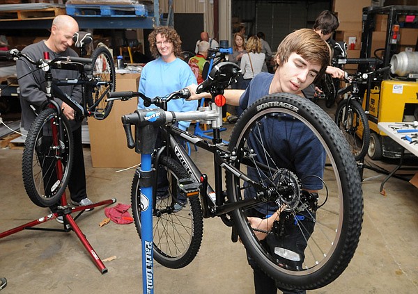 Martin Johnson, right, mechanic with Phat Tire, checks the brakes and gear alignment of a bicycle Wednesday at AMP Sign and Banner in Bentonville as volunteers assemble new bikes purchased for the Bentonville School District. The district received grants from the Walton Family Foundation, Coca-Cola, Bentonville Public Schools Foundation and the Walmart Visitors Center to purchase 540 bicycles and Bell donated 540 helmets to accompany the bikes. Each school will have 30 bicycles to use with their physical education classes. 
