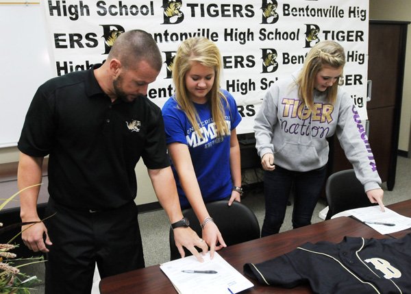 Kent Early, head coach, from left, shows Anna Thomas and Kate Lacina, softball players from Bentonville, where to sign on their letters of intent Thursday at Tiger Athletic Complex. Thomas and Lacina signed to play at University of Memphis and Ouachita Baptist University, respectively. 