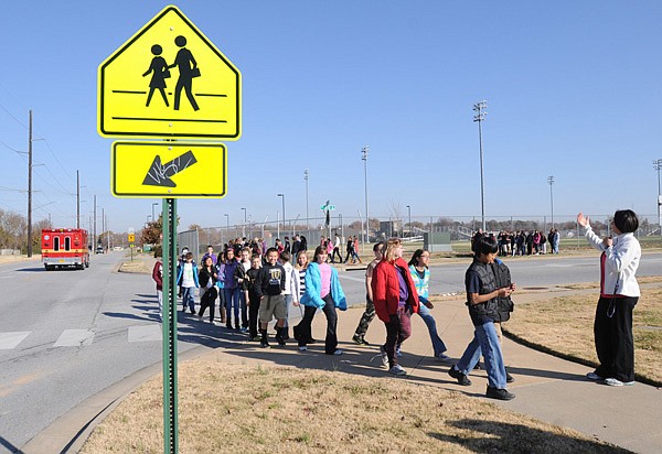 Heather Coon, right, Ruth Hale Barker Middle School physical education teacher, directs sixth-graders Friday across Southeast 18th Street in Bentonville. The students were taking a walk around the school and learning crosswalk safety from teachers. 
