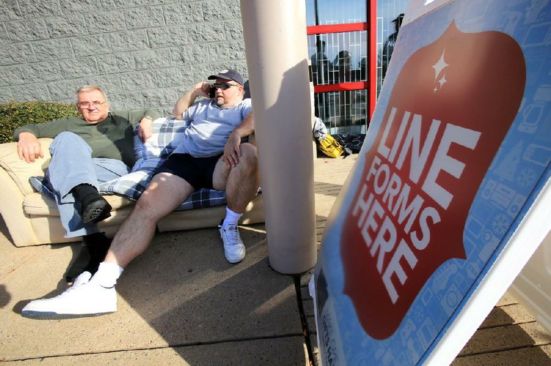 Larry Foshee (right) of Little Rock talks on the phone Thursday afternoon as he waits in line outside Best Buy in west Little Rock with friend Zbyszek Blaszko of Poland for the store to open at midnight. 