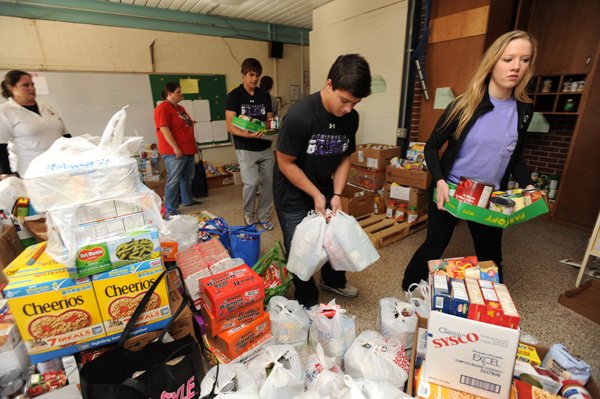 Natalie Counce, right, a junior at Fayetteville High School, and sophomore Nico Suarez, center, help unload canned food items Nov. 16 at the Jefferson Center after a food drive at Holcomb Elementary and Owl Creek schools to support The Outback’s annual holiday basket project in Fayetteville. 