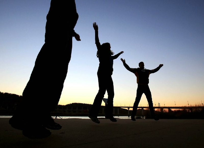 Ajay Mishra (from left) of Arkansas Regional Organ Recovery Agency, Bernadette Rhodes of North Little Rock’s Fit 2 Live program and Jeremy Rhodes do jumping jacks while playing with fitness dice during the health fair Sunday evening before the Big Dam Bridge Full Moon Walk.