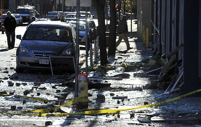 People walk through debris Saturday about a block from the site of a Friday evening explosion in Springfield, Mass. 
