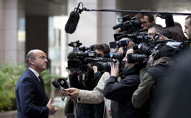 Spain’s Economy Minister Luis de Guindos (left) speaks with the media Monday as he arrives for a meeting of eurogroup finance ministers at the EU Council building in Brussels. 