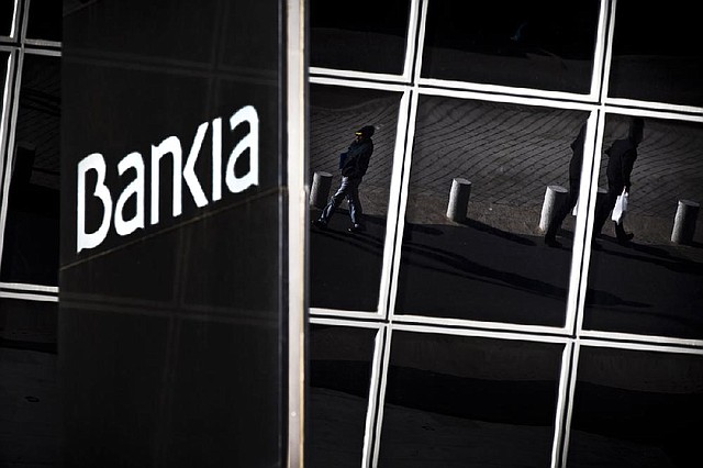 Pedestrians are reflected in windows of the Bankia bank headquarters in Madrid on Wednesday. European Union authorities approved almost $48 billion in bailout loans for four of Spain’s struggling banks, including $23 billion for Bankia. 