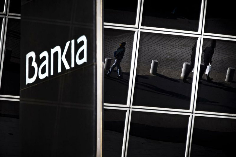 Pedestrians are reflected in windows of the Bankia bank headquarters in Madrid on Wednesday. European Union authorities approved almost $48 billion in bailout loans for four of Spain’s struggling banks, including $23 billion for Bankia. 