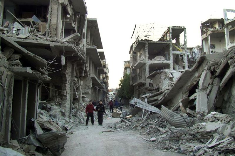 Syrians walk Thursday on a street in Homs province that was hit Wednesday by government bombs.


