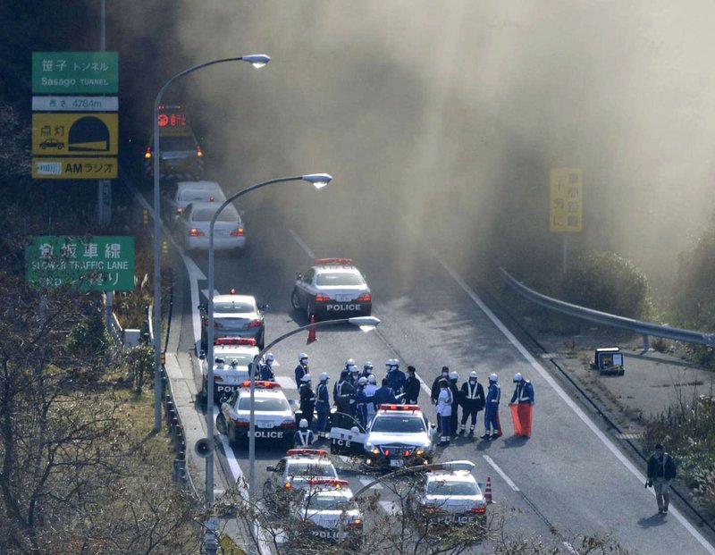 Police vehicles are parked at the entrance as smoke billows out of the Sasago Tunnel on the Chuo Expressway in Koshu, Yamanashi Prefecture, central Japan, Sunday morning, Dec. 2, 2012. A part of the tunnel collapsed Sunday morning, possibly involving several vehicles and injuring several people, local media said.