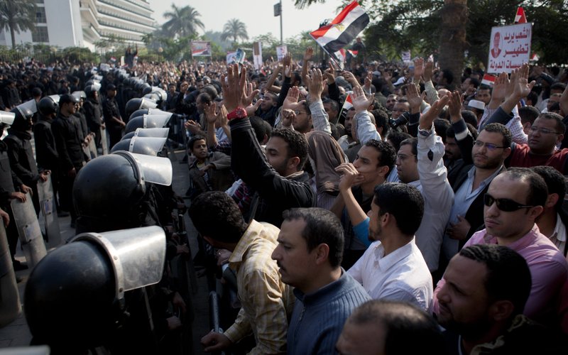 Supporters of Egyptian President Mohammed Morsi chant slogans as riot police, left, stand guard in front of the entrance of Egypt’s top court, in Cairo, Egypt, Sunday, Dec. 2, 2012. Egypt’s top court announced on Sunday the suspension of its work indefinitely to protest “psychological and physical pressures,” saying its judges could not enter its Nile-side building because of the Islamist president’s supporters gathered outside. Arabic on the poster, right, reads, "The people want to purify the state's institutions."