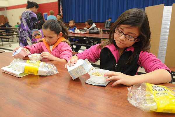 Jocelyn Martinez, 6, left, and big sister Vasti Martinez, 9, pour milk over their Frosted Flakes on Friday at Bayyari Elementary School in Springdale while eating breakfast before school. Beginning Monday, Bayyari will be the first of five Springdale elementary schools to participate in Breakfast in the Classroom, a program sponsored by the Walmart Foundation, which provides free breakfast for all students in the school. 