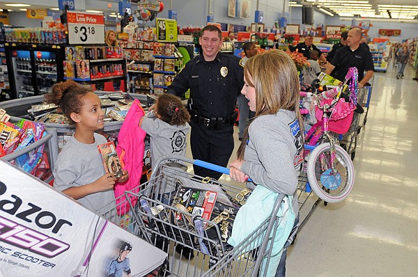 Liliana Cunningham, 6, left, shows Mindy Medina, police dispatcher, right, a movie she may want to purchase Monday at Walmart Supercenter on South Walton Boulevard in Bentonville. Officers and other police personnel shopped with 29 students during the Bentonville Fraternal Order of Police’s annual Shop with a Cop event. Students had a budget of about $250 each to spend on presents for family members, teachers, loved ones, friends and themselves. 