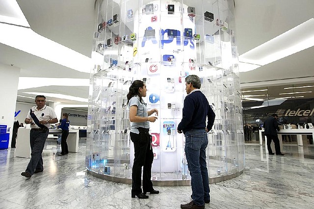 An America Movil SAB Telcel employee helps a customer at a store in Mexico City. Recent rulings and orders have cut into the wireless phone service provider’s profitability. 