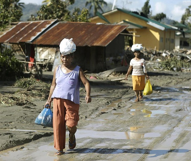 Residents affected by Tuesday’s storm walk back to their homes Thursday after receiving relief supplies in New Bataan township in the southern Philippines. 